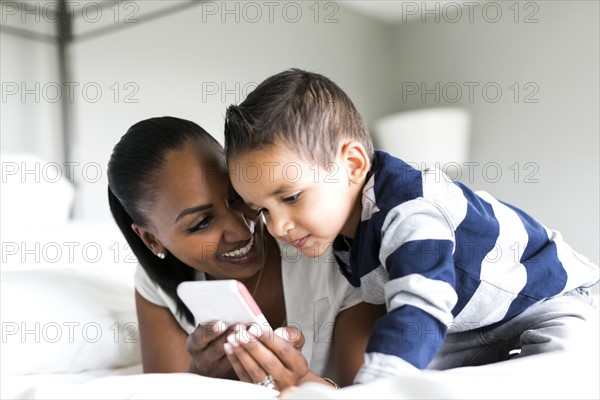 Mother and son (2-3) lying on bed and using smart phone