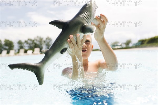 Boy (6-7) playing with toy shark in swimming pool