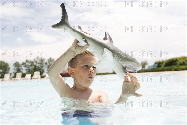 Boy (6-7) playing with toy shark in swimming pool