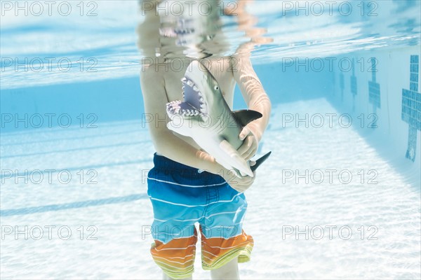 Boy (6-7) playing with toy shark in swimming pool