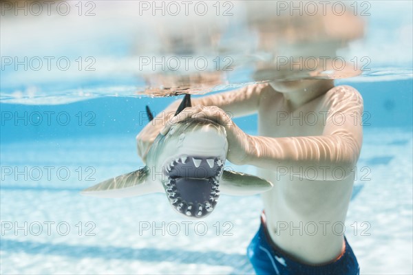 Boy (6-7) playing with toy shark in swimming pool