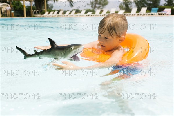 Boy (6-7) playing with toy shark in swimming pool