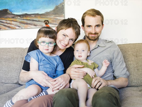 Portrait of parents with daughters (12-17 months, 2-3) sitting on sofa