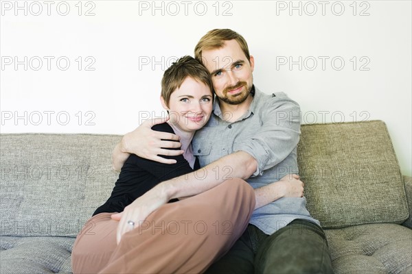 Couple looking at camera and embracing on sofa