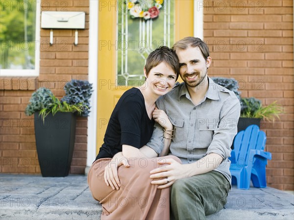 Happy couple sitting in front of house