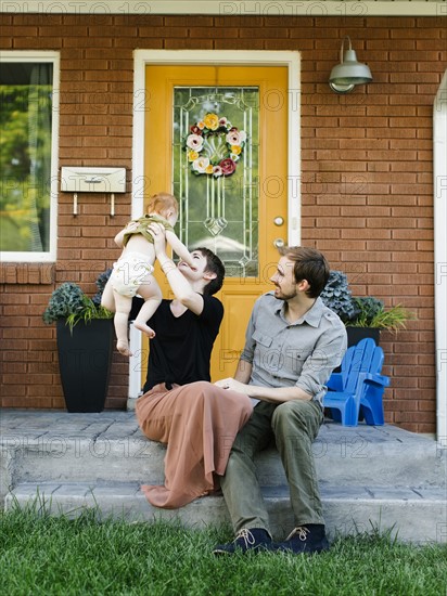 Parents with daughter (12-17 months) sitting in front of house