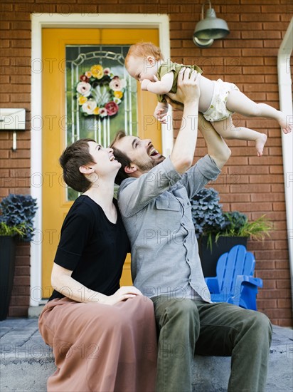 Parents with daughter (12-17 months) sitting in front of house