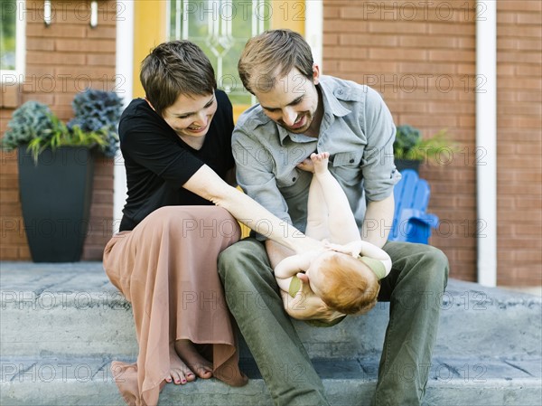 Parents with daughter (12-17 months) sitting in front of house