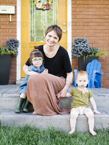 Mother with daughters (2-3, 12-17 months) sitting in front of house