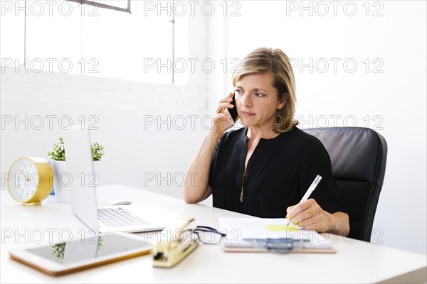 Woman using mobile phone, looking at laptop