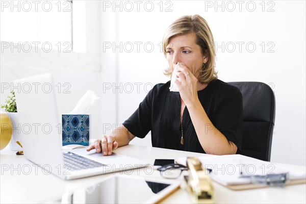 Woman using laptop, blowing nose