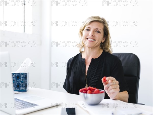 Woman sitting in office, eating raspberries