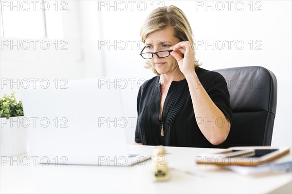 Mature woman in office touching her eyeglasses