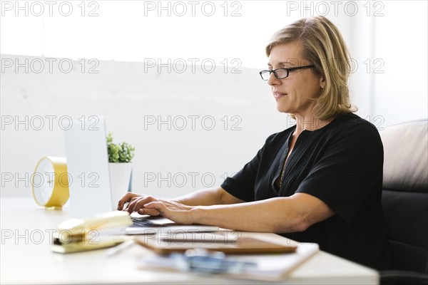 Mature woman in office typing on laptop