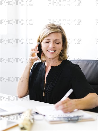 Mature woman talking on mobile phone and taking notes