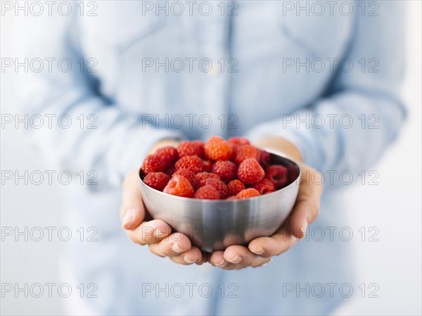 Mid section of Mature woman holding bowl with raspberries