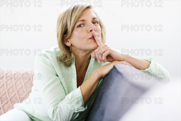 Portrait of woman sitting on sofa with finger on lips