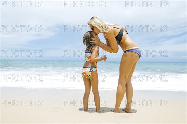 Mother kissing daughter (6-7) on beach