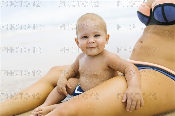 Baby boy (12-17 months) sitting between legs of her mother