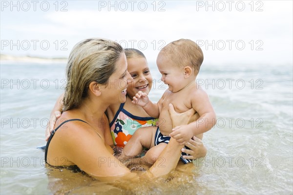 Mother playing with children (6-7, 12-17 months) in sea