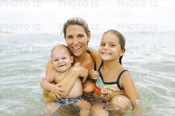 Mother and children (6-7, 12-17 months) embracing in sea