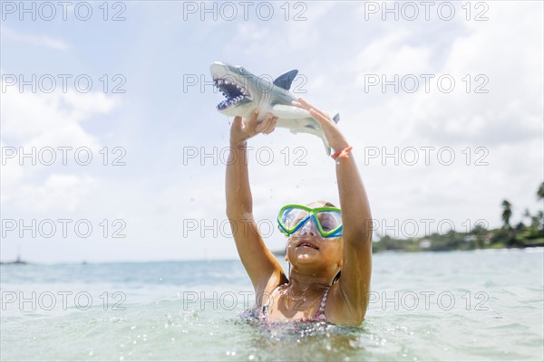 Girl (6-7) playing with shark toy in sea