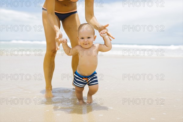 Son (12-17 months) learning to walk with mother on beach