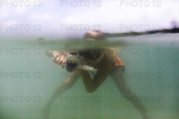 Boy (8-9) playing with toy shark in sea