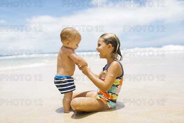 Sister (6-7) holding brother (12-17 months) on beach