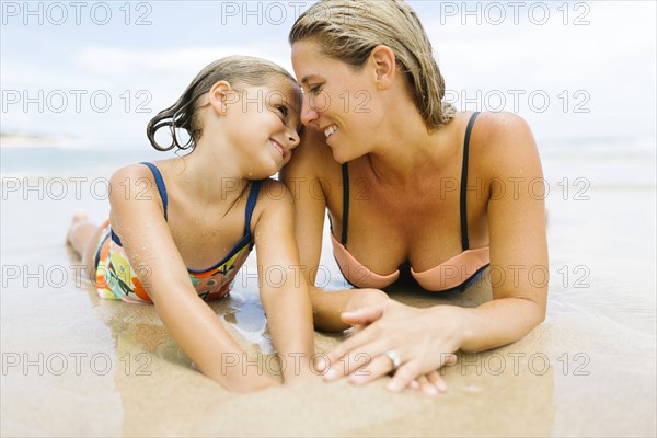 Mother lying with daughter (6-7) on beach