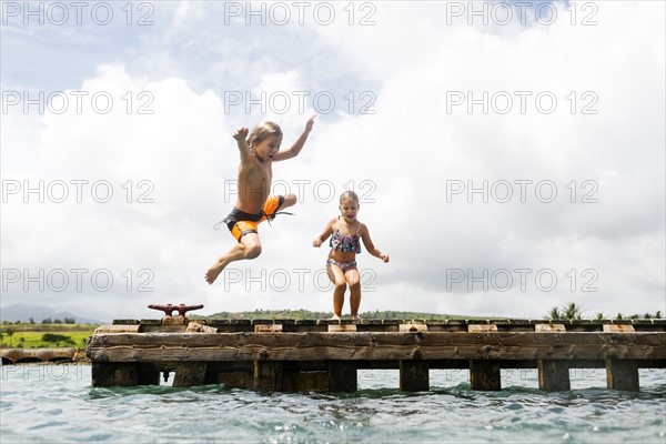 Boy (8-9) and girl (6-7) jumping into sea from jetty