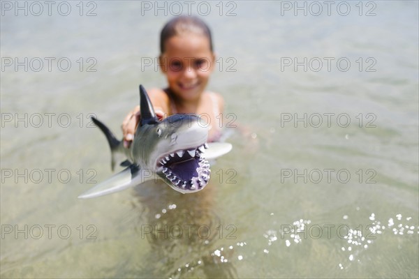 Girl (6-7) playing with toy shark in sea