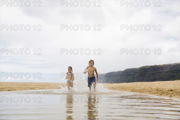 Boy (8-9) and girl (6-7) running through sea