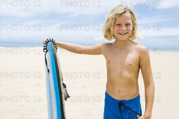 Boy (8-9) standing on beach and holding surfboard
