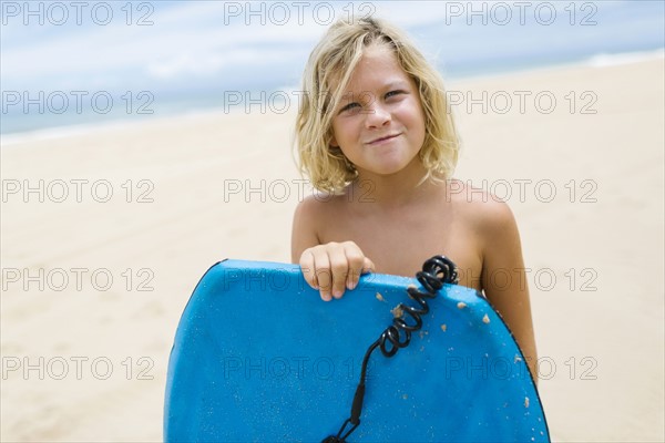 Boy (8-9) standing on beach and holding surfboard