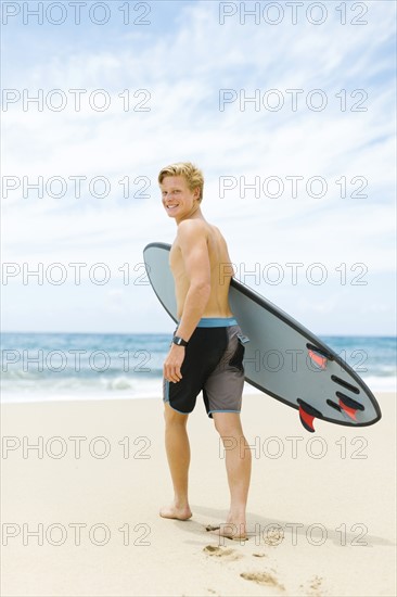 Man walking on beach and holding surfboard