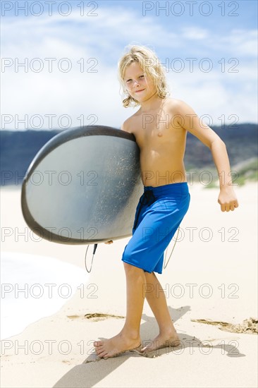 Boy (8-9) standing on beach and holding surfboard