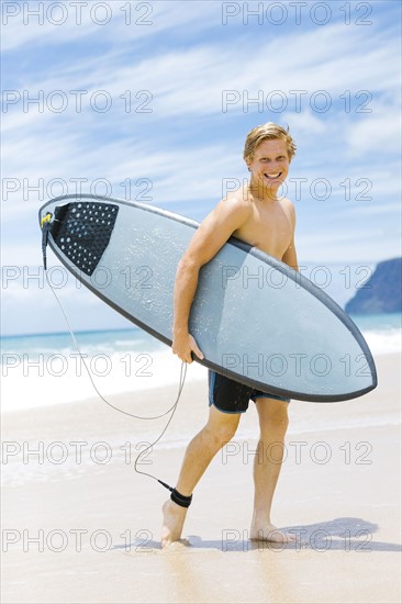 Man walking on beach and holding surfboard