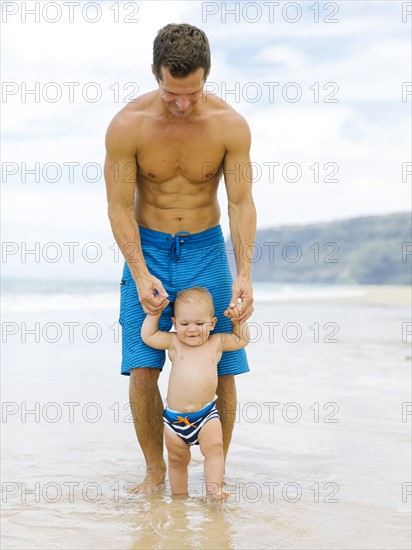 Son (12-17 months) learning to walk with father on beach