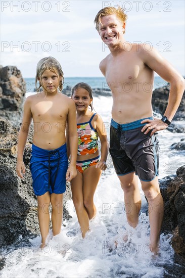 Man and children (6-7, 8-9) standing between rock in sea