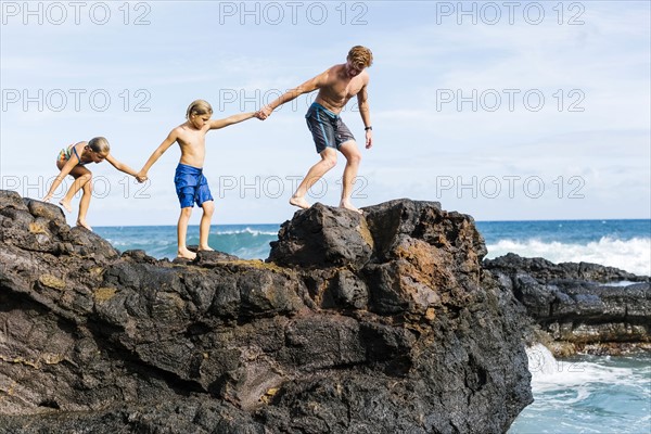 Man and children (6-7, 8-9) walking on rock by sea