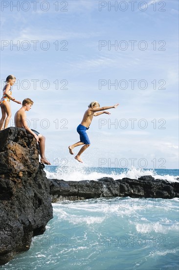 Man and girl (6-7) resting on cliff and boy (8-9) jumping