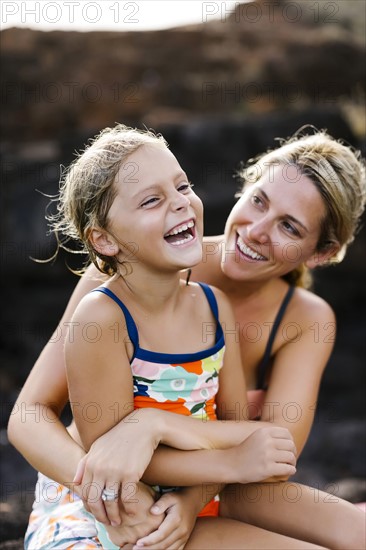 Mother and daughter (6-7) embracing with rock in background