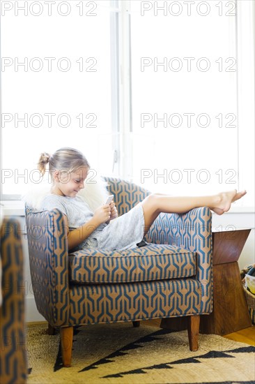 Young girl (6-7) sitting on armchair and using mobile phone