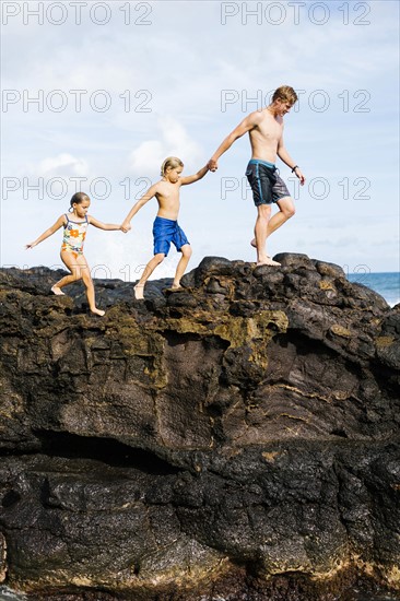 Young man walking on rock with kids (6-7, 8-9)