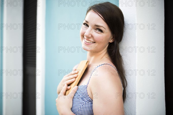 Cheerful woman with digital tablet leaning against building wall