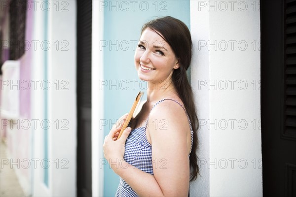 Cheerful woman with digital tablet leaning against building wall