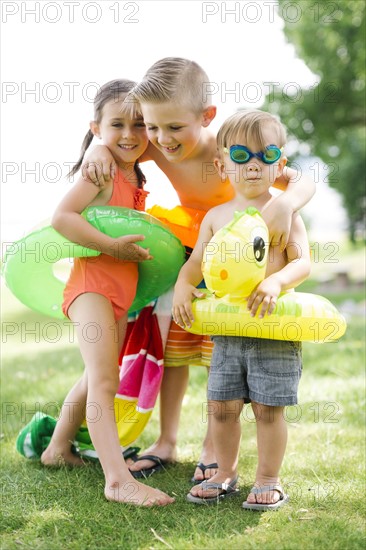 Two boys (2-3, 6-7) and girl (4-5) standing with inflatable rings