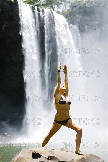 USA, Hawaii, Kauai, Woman practicing yoga next to waterfall