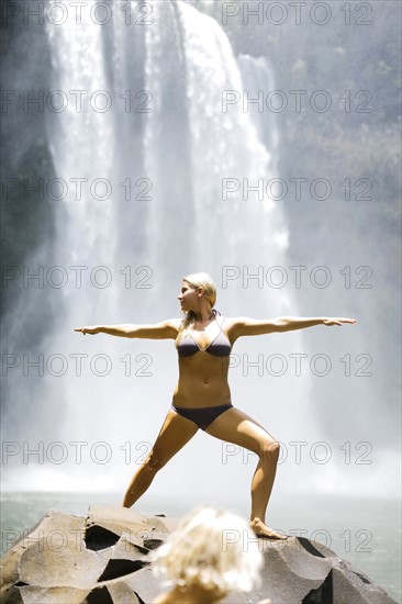 USA, Hawaii, Kauai, Woman practicing yoga next to waterfall